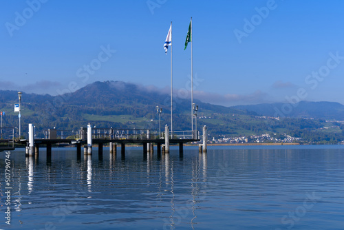 Scenic landscape with Lake Zürich and pier with flags seen from City of Rapperswil-Jona on a sunny spring day. Photo taken April 28th, 2022, Rapperswil-Jona, Switzerland.