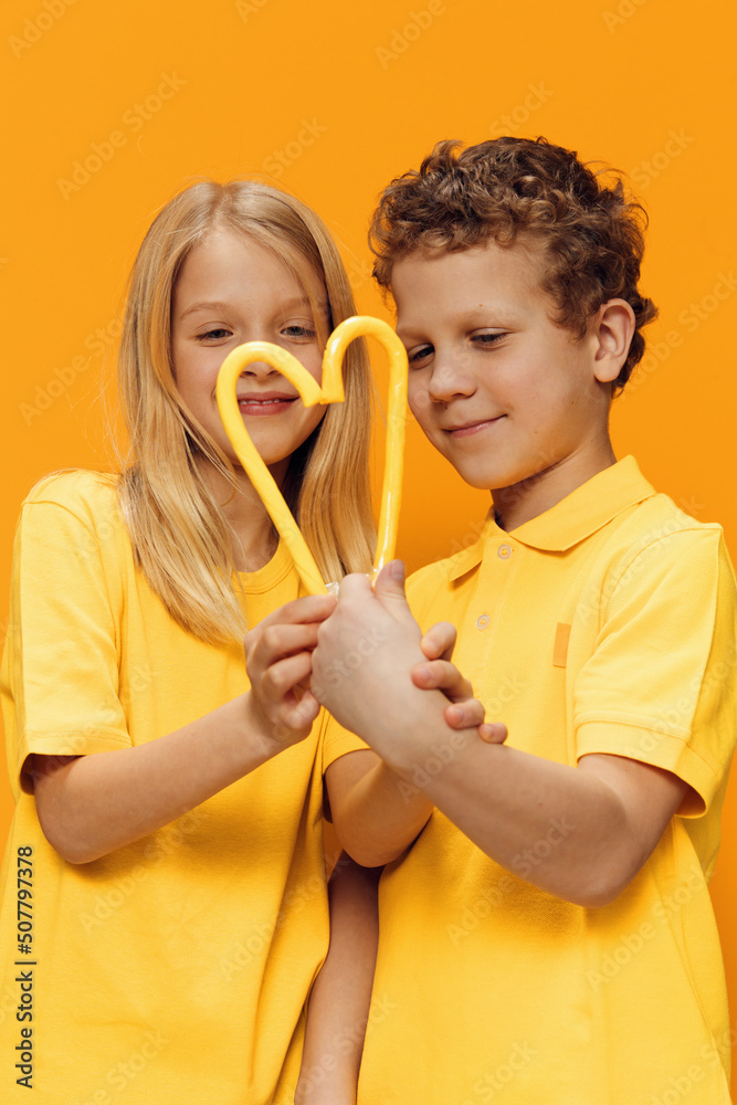 Fototapeta premium cute, happy children brother and sister, stand in bright clothes and put their candies to each other to form a heart shape. photo with empty space for advertising insert