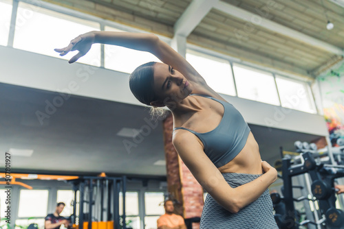 Beautiful brunette caucasian woman in her 20s stretching her back at the gym. Flexibility and mobility concept. . High quality photo
