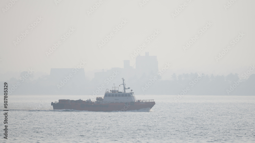 Boat sailing on a misty morning close to the shore against an urban city background.