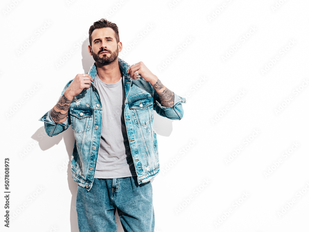 Portrait of handsome confident stylish hipster lambersexual model. Sexy man dressed in jeans jacket. Fashion male isolated on white wall in studio Portrait of handsome confident stylish hipster lambersexual model. Sexy man dressed in jeans jacket. Fashion male isolated on white wall in studio