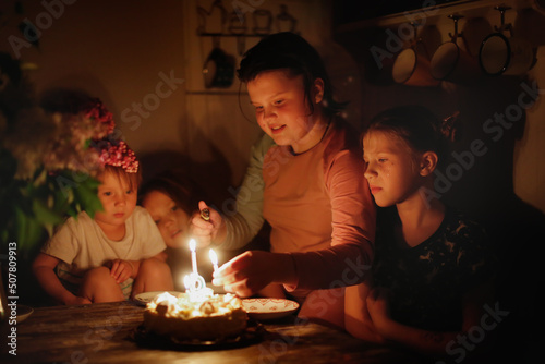 Cute child girl at table with birthday cake with siblings  dark style. Cake and candle 9 years birthday celebration