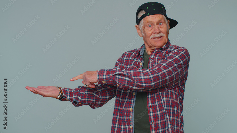 Handsome senior man showing thumbs up and pointing empty place, advertising area for commercial text, copy space for goods promotion. Elderly grandfather. Studio shot indoors on gray wall background Handsome senior man showing thumbs up and pointing empty place, advertising area for commercial text, copy space for goods promotion. Elderly grandfather. Studio shot indoors on gray wall background
