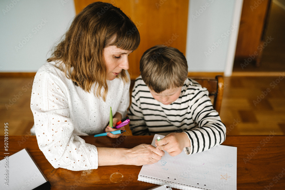 High angle view of mother teaching son with down syndrome to draw in book at table High angle view of mother teaching son with down syndrome to draw in book at table