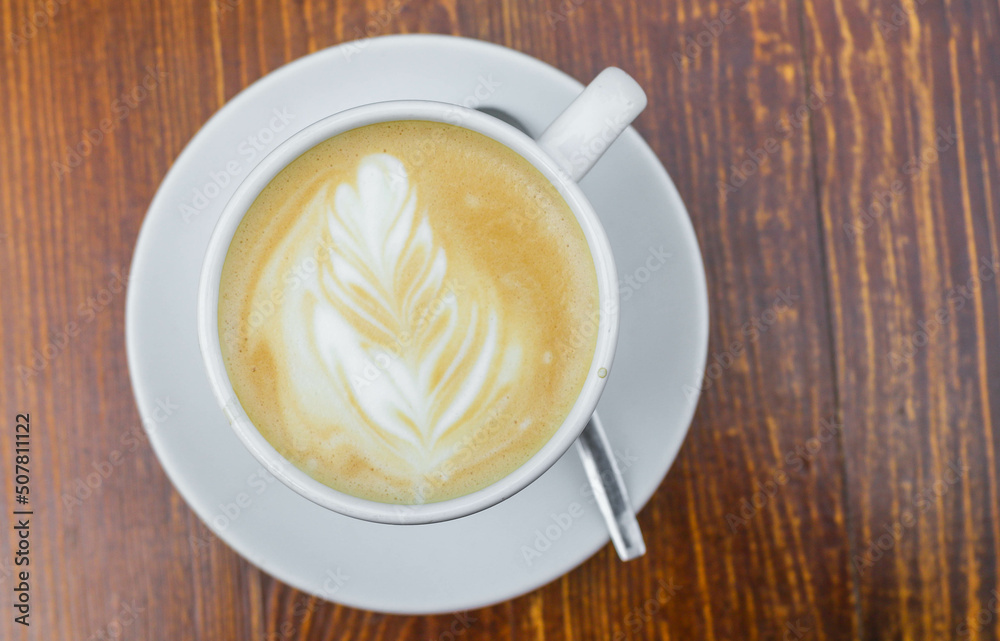 There is a cup of coffee on a wooden brown table during the day There is a cup of coffee on a wooden brown table during the day