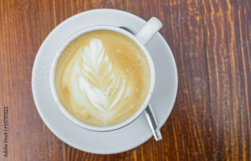 There is a cup of coffee on a wooden brown table during the day