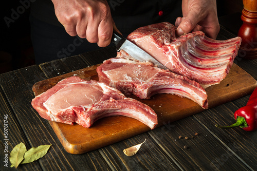 The chef cuts raw meat. Butcher cutting pork ribs. Meat with bone on a wooden cutting board. National cuisine.