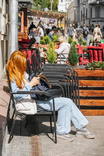 Unrecognizable young girl sitting in armchair near street cafe and using smartphone. Modern technologies