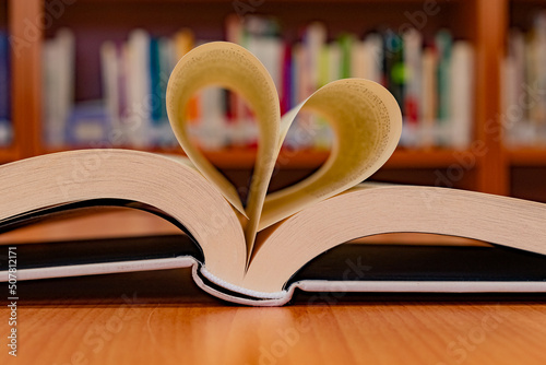 Obraz na plátně Close-up of an open book with its pages in the shape of a heart, on the table of a reading room in a library