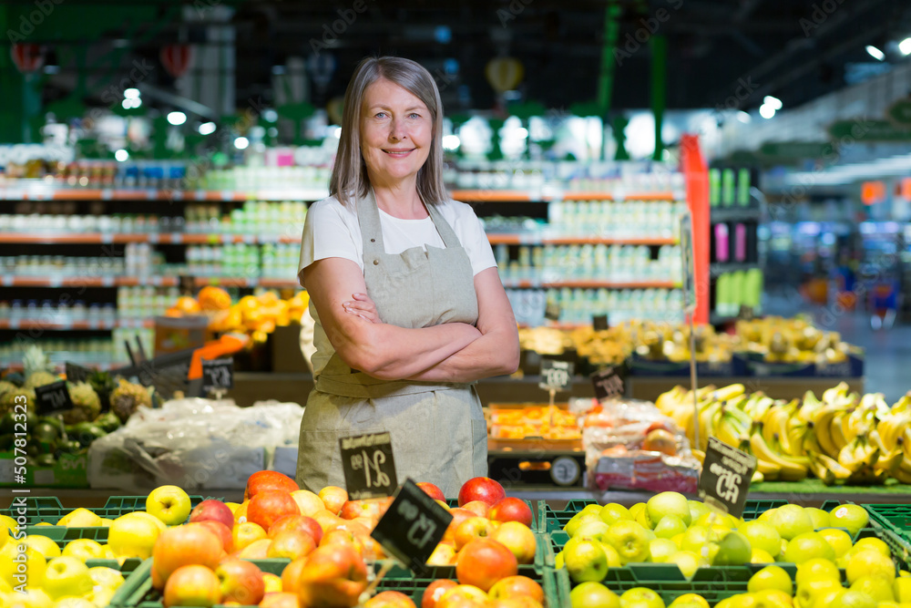 Portrait of senior woman manager of grocery store, supermarket. Standing in work clothes, arms crossed, looking at the camera, smiling