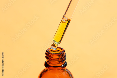 A drop of liquid falling from a pipette into an amber bottle. Skincare products, natural cosmetic on orange background. Beauty concept for face and body care.