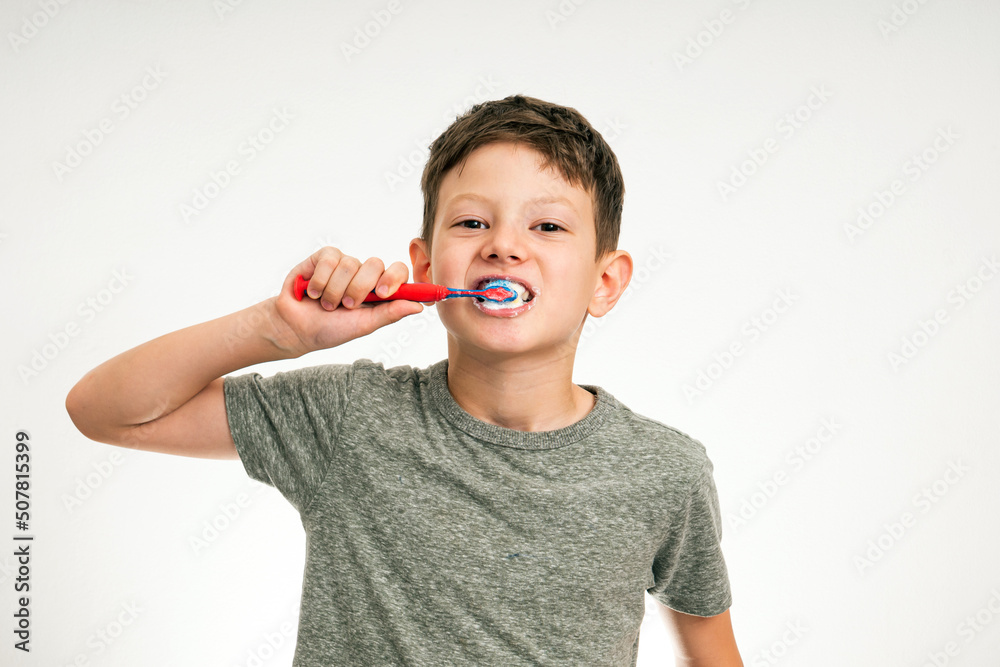 Little boy cleaning teeth with toothbrush and toothpaste on studio white background. Perfect removing plaque with red toothbrush Little boy cleaning teeth with toothbrush and toothpaste on studio white background. Perfect removing plaque with red toothbrush