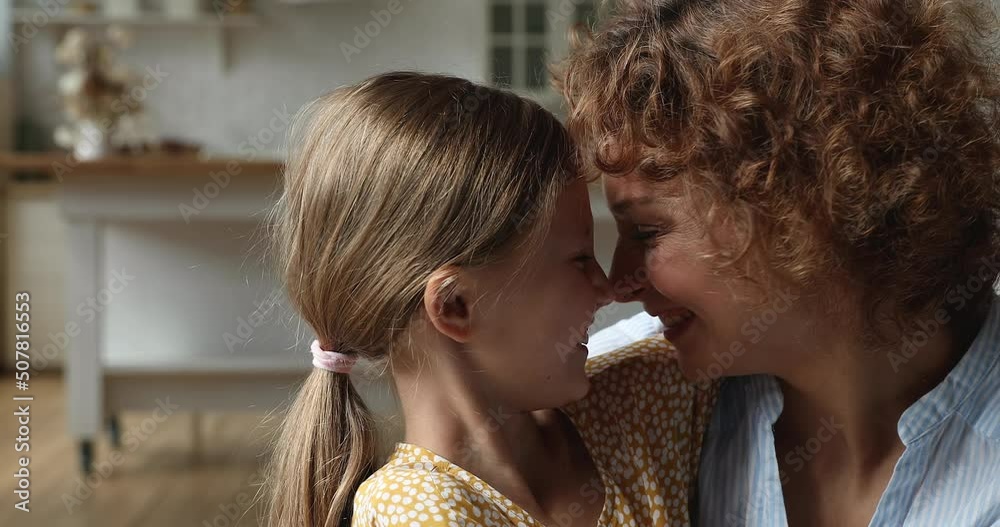 Close up head shot adorable little 7s child girl cuddling affectionate young mother, showing sincere feelings, touching noses missing after long separation, enjoying tender sweet family time at home.