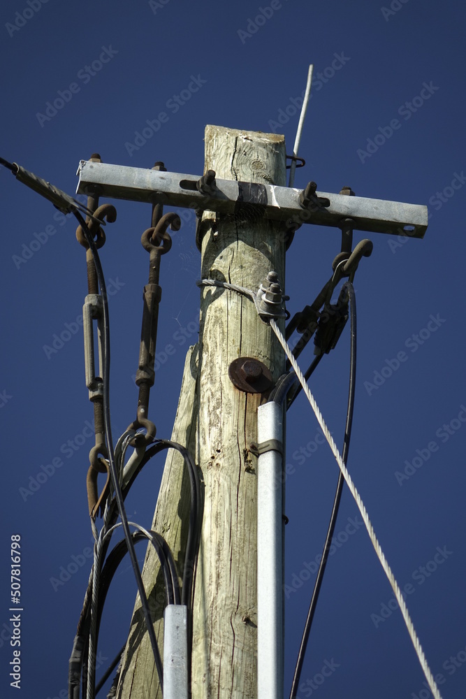 Wires and top of old wooden telegraph pole plus small cobbweb on the right side under a blue spring sky, concept: vintage, use: background, wallpaper (vertical), Sehnde, Lower Saxony, Germany Wires and top of old wooden telegraph pole plus small cobbweb on the right side under a blue spring sky, concept: vintage, use: background, wallpaper (vertical), Sehnde, Lower Saxony, Germany