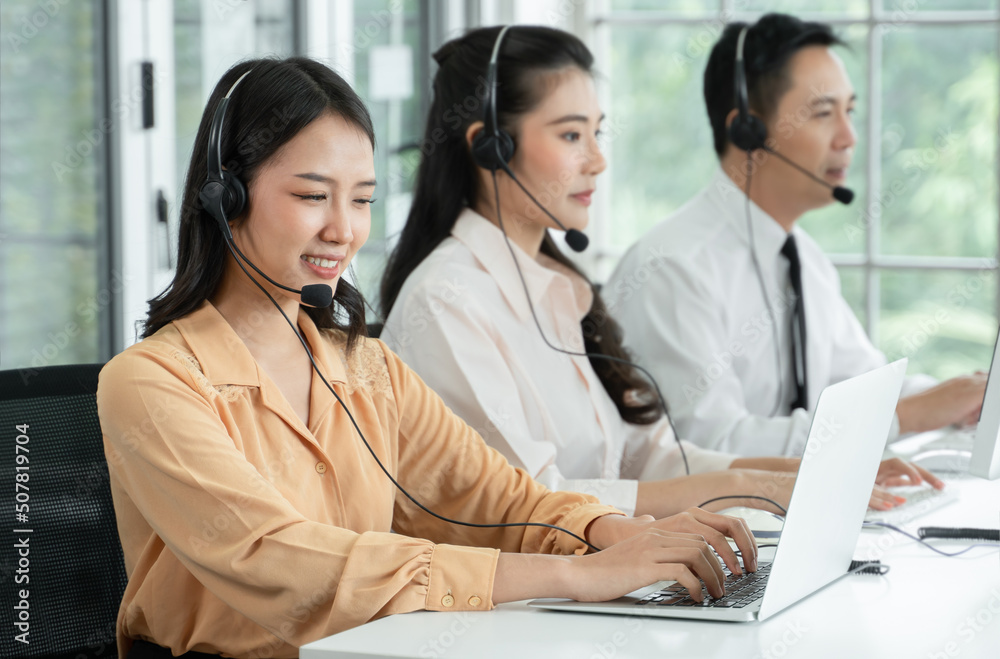 Group of Asian employee work in telemarketing customer service teams. Young operator woman working with headset smiling and doing customer support at work. Call Center with service mind concept Group of Asian employee work in telemarketing customer service teams. Young operator woman working with headset smiling and doing customer support at work. Call Center with service mind concept