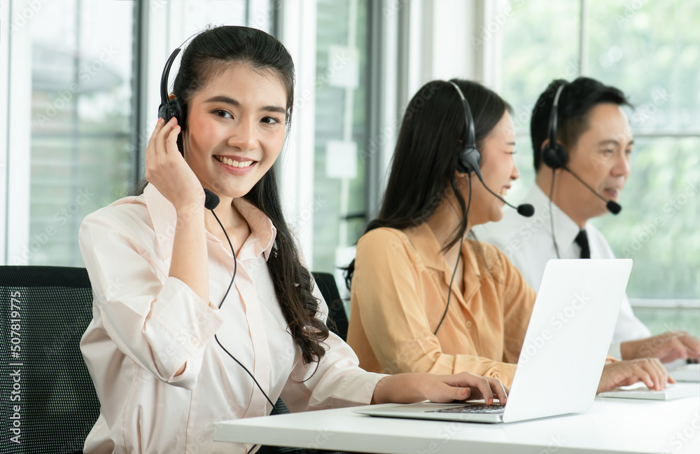 Group of Asian employee work in telemarketing customer service teams. Young operator woman working with headset smiling and doing customer support at work. Call Center with service mind concept Group of Asian employee work in telemarketing customer service teams. Young operator woman working with headset smiling and doing customer support at work. Call Center with service mind concept