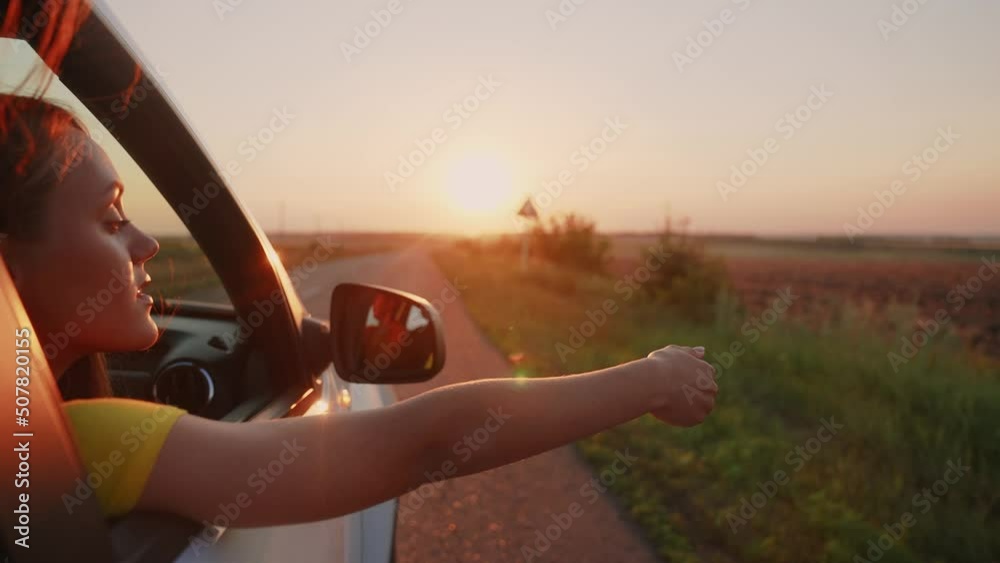 travel by car concept. the girl put her hand in the car window at sunset. freedom road a drive concept. girl travel by car sun goes on vacation on the road at sunset. summer adventure