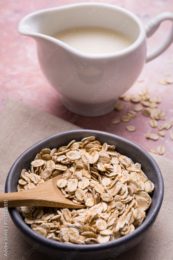 In the foreground, bowl with wholemeal oats for breakfast. in the background, pitcher with organic oat vegetable drink. In the foreground, bowl with wholemeal oats for breakfast. in the background, pitcher with organic oat vegetable drink.