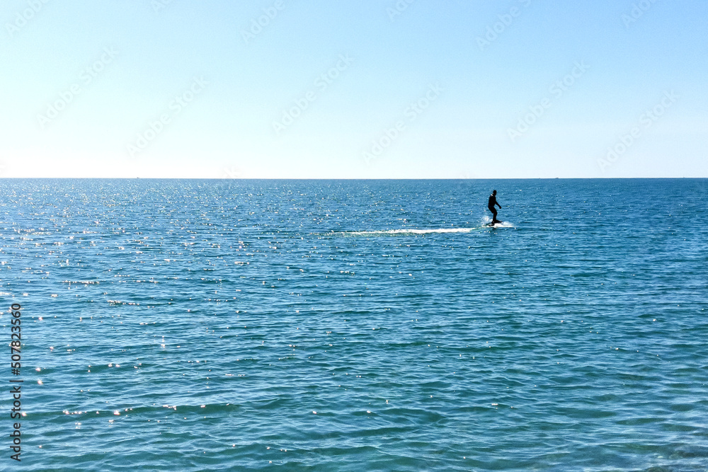 Man surfing on hydrofoils. Silhouette on the background of the sea surface on a bright sunny day