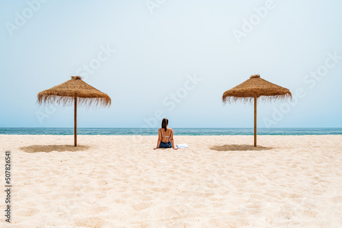 Female traveler sitting on sand near ocean