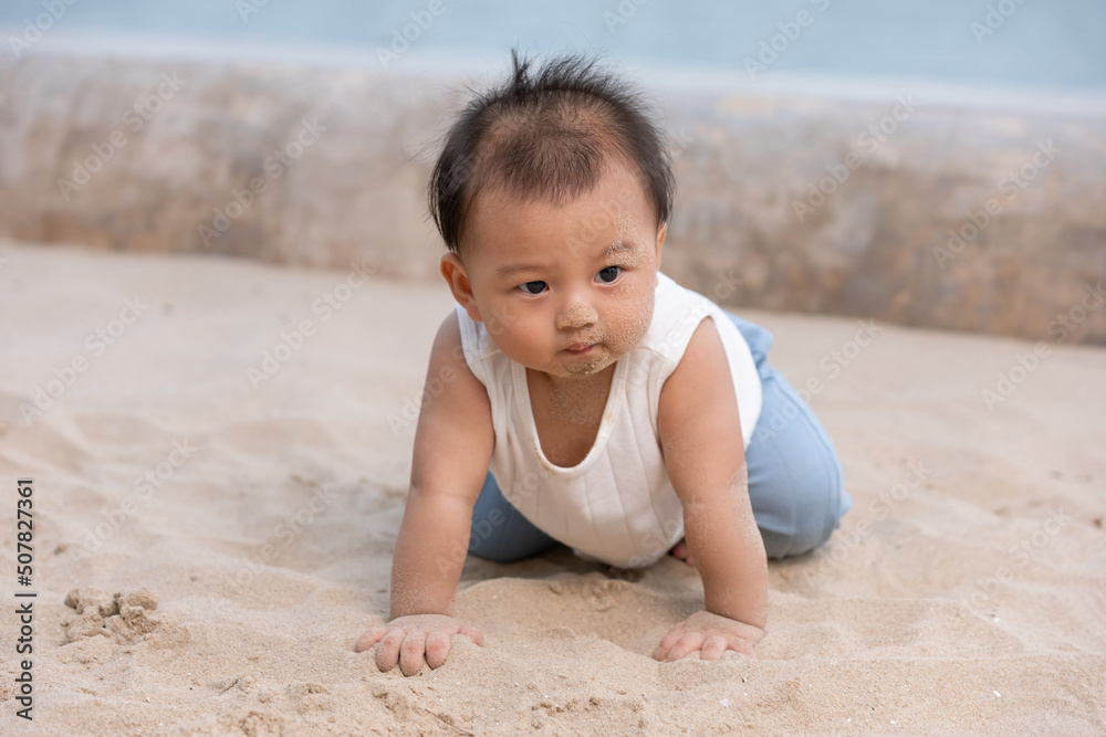 Healthy asian baby toddler crawling on the beach to learn to crawl outdoors. Adorable baby keeping her belly and legs down on sand to belly crawl fun and happiness at home. Baby growth concept Healthy asian baby toddler crawling on the beach to learn to crawl outdoors. Adorable baby keeping her belly and legs down on sand to belly crawl fun and happiness at home. Baby growth concept
