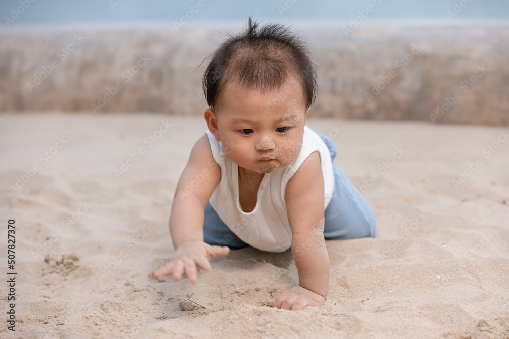 Healthy asian baby toddler crawling on the beach to learn to crawl outdoors. Adorable baby keeping her belly and legs down on sand to belly crawl fun and happiness at home. Baby growth concept Healthy asian baby toddler crawling on the beach to learn to crawl outdoors. Adorable baby keeping her belly and legs down on sand to belly crawl fun and happiness at home. Baby growth concept