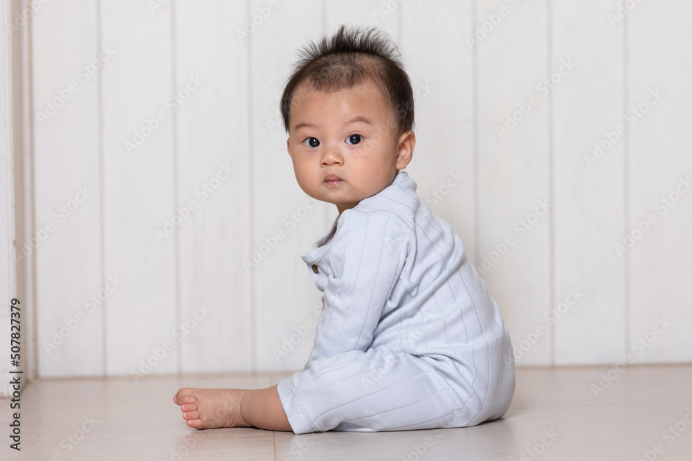 Healthy asian baby toddler sitting on floor to learn to crawl indoors looking at camera. Adorable baby looking around on the floor indoors at home Healthy asian baby toddler sitting on floor to learn to crawl indoors looking at camera. Adorable baby looking around on the floor indoors at home
