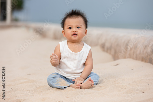 Adorable asian baby sit on sand spend time to learn all around beach and sea. First time to touch sand of cute baby infant excite and happiness. Little baby boy playing outdoor and looking at camera