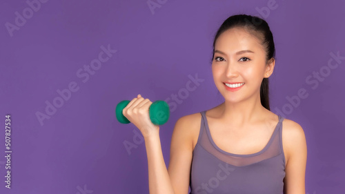 Fitness woman doing workout with weights dumbbell , Beautiful Asian brunette woman cute girl smile in sportswear exercising isolated on purple background