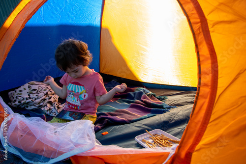 A child sits in a tent on the lakeshore, watches cartoons on the phone and eats sweets, a girl sits in a tent, tourism, family, summer, vacation, picnic, travel