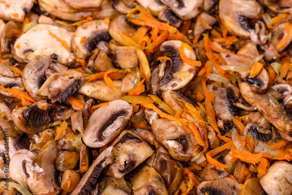 Fried champignons with carrots, onions and spices in a pan against a dark concrete background