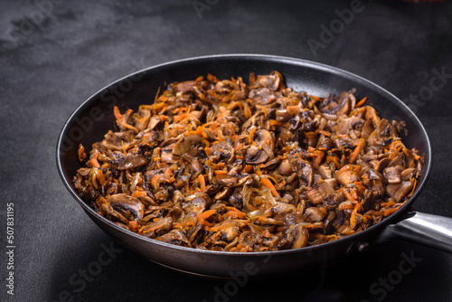 Fried champignons with carrots, onions and spices in a pan against a dark concrete background