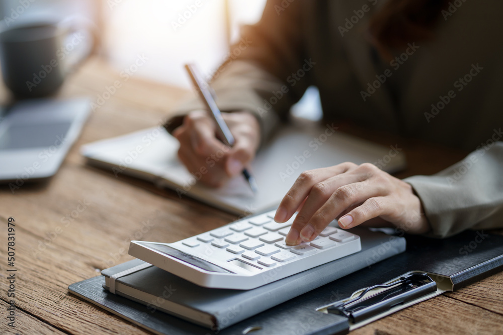 Close-up of businesswoman hands using a calculator to check company finances and earnings and budget. Business woman calculating monthly expenses, managing budget, papers, loan documents, invoices. Close-up of businesswoman hands using a calculator to check company finances and earnings and budget. Business woman calculating monthly expenses, managing budget, papers, loan documents, invoices.