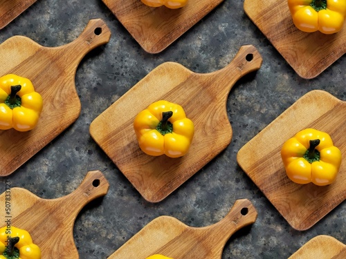 Pattern of yellow sweet pepper on wooden cutting board on black concrete background. Rustic flatlay with spring vegetables.
