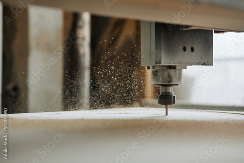 Macro shot of CNC engraving machine cutting wood in automated production workshop with sawdust flakes in air, copy space