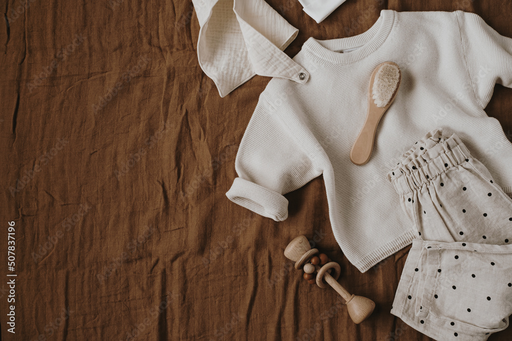 Stylish elegant newborn baby clothes and accessories on neutral brown linen cloth. Sweater, joggers, hat, muslin bib, brush. Online fashion store, online shopping branding concept. - obrazy, fototapety, plakaty 