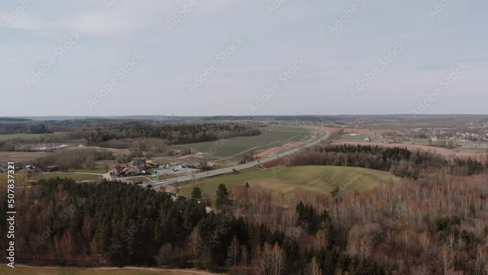 Aerial view of countryside on spring day. Small manicured agricultural fields surrounded by coniferous trees and birches. Cars are driving along highway. Houses and gas station in the village. Aerial view of countryside on spring day. Small manicured agricultural fields surrounded by coniferous trees and birches. Cars are driving along highway. Houses and gas station in the village.