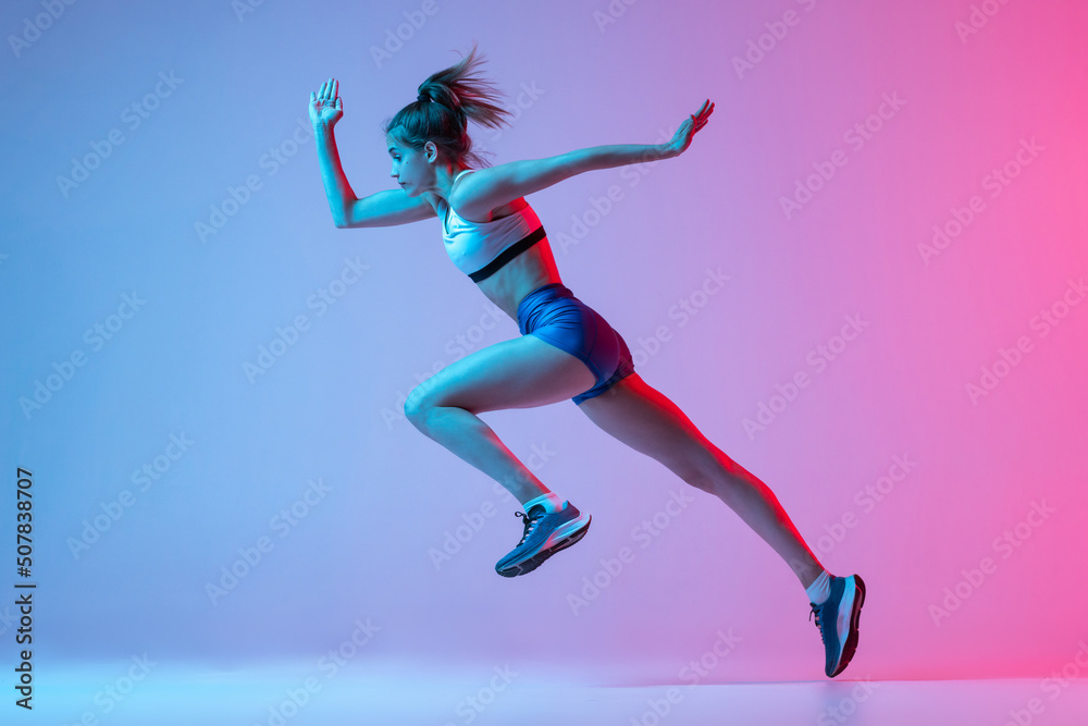 Studio shot of professional female athlete, runner training isolated on pink studio background with blue neon filter, light. Concept of action, motion, speed