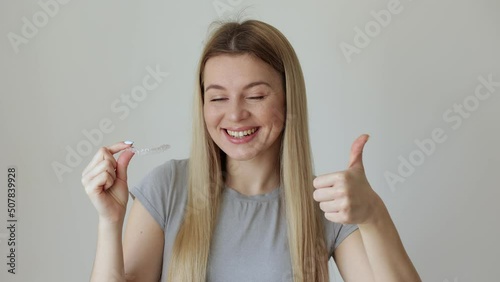 Happy young woman holding an invisible braces aligner and rising thumb up, recommending this new treatment. Dental healthcare concept. photo