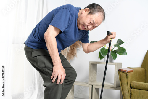 膝を押さえながら杖をつく高齢者男性