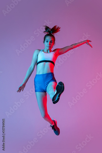 Training in long jump sport. Young girl, female athlete practicing isolated on pink studio background with blue neon filter, light. Concept of action, motion, speed