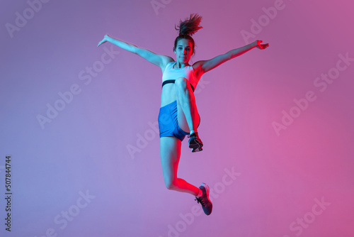 Moments. Young girl, female athlete training long jump technique isolated on pink studio background with blue neon filter, light. Concept of action, motion, speed © master1305