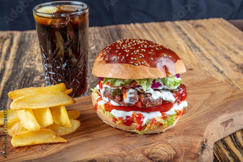 Juicy and appetizing burger with tomatoes, lettuce, cucumber, melted cheese and onions with brioche bun served on a wooden board with fries