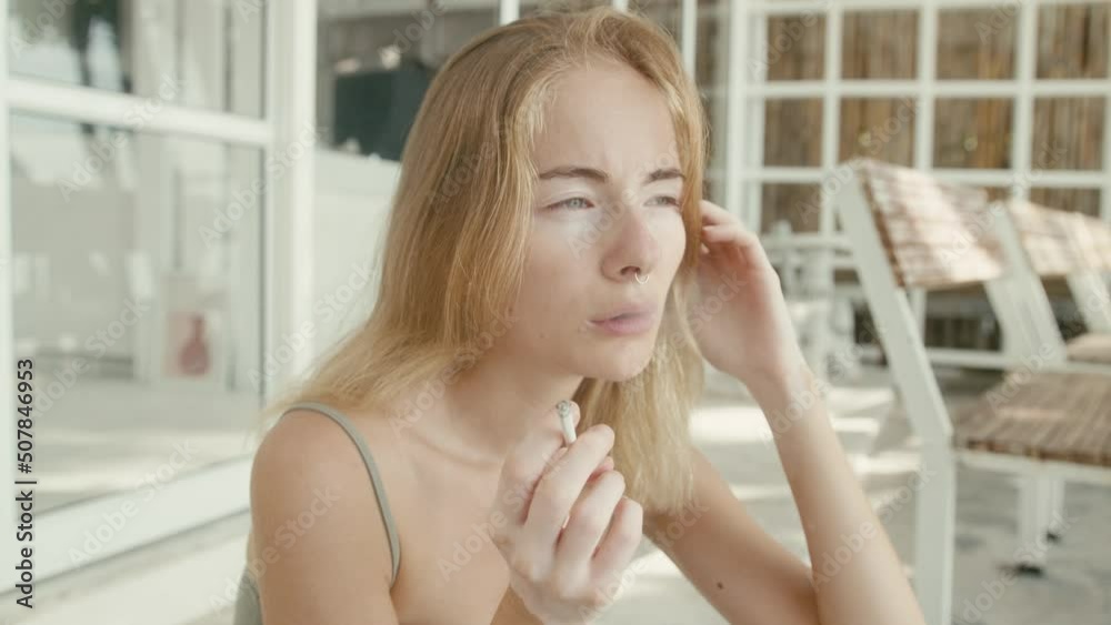 Pretty young woman with vitiligo pigmentation sits on the stairs and smokes 