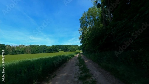 FPV DRONE - REVERSE SHOT flight over dirt road, close to green field photo