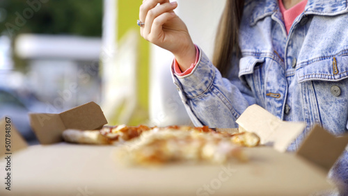 Beautiful woman eating pizza on street. Media. Woman snacking on pizza for lunch outside cafe. Young woman eats pizza on background of busy city