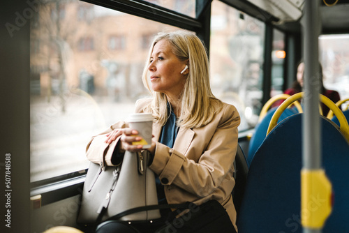 Businesswoman looking through window holding disposable cup while commuting in bus photo