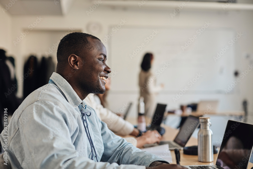 Side view of smiling male student with laptop in classroom Side view of smiling male student with laptop in classroom