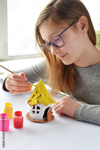 Girl making toys with your own hands, paints a clay house with gouache. Indoors creative leisure for children. Supporting creativity, learning by doing, DIY project, hand craft. Master class of art