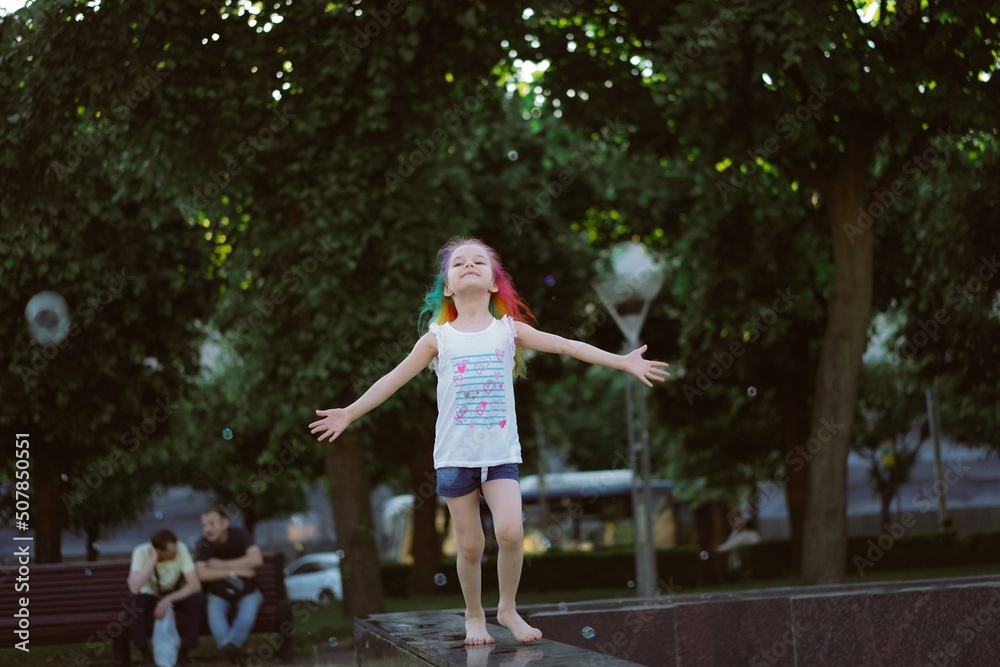 Φωτογραφία pretty little girl with colorful dyed hair holding bunch of baloons running along fountain parapet
